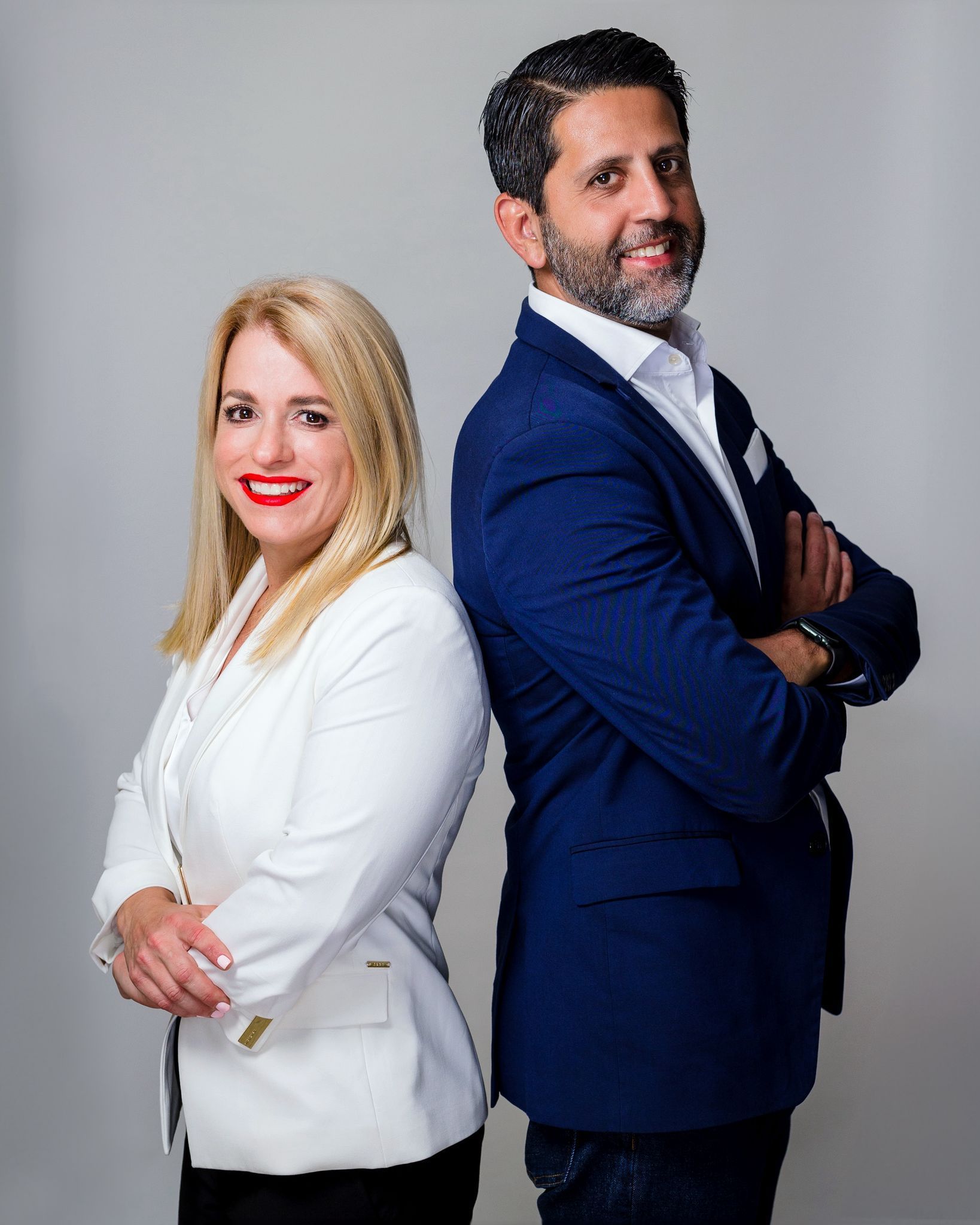 Two professionals standing back-to-back, one in a white blazer and one in a blue suit, against a gray background