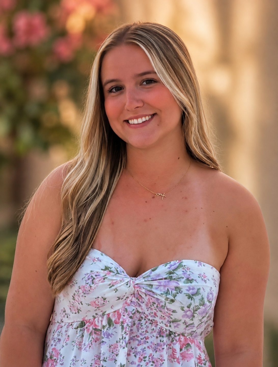 Smiling woman in a floral strapless dress standing outdoors with a blurred garden background