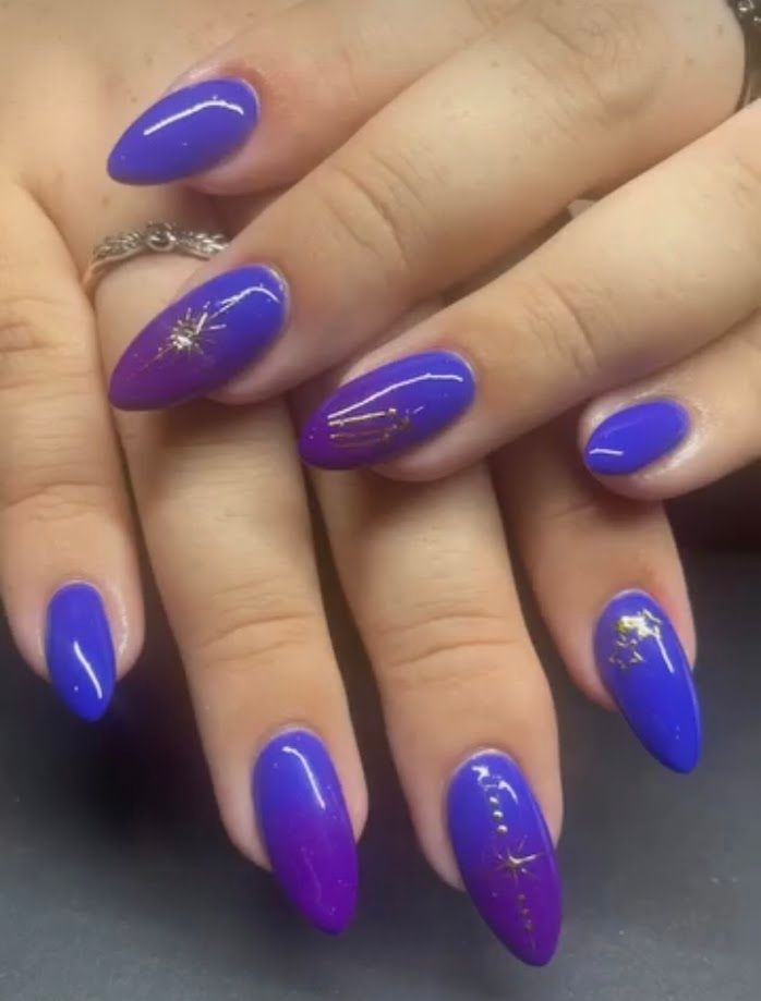 Purple stiletto nails with gold glitter accents on crossed hands