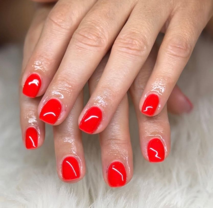 Hands with glossy bright red manicure on a soft white background