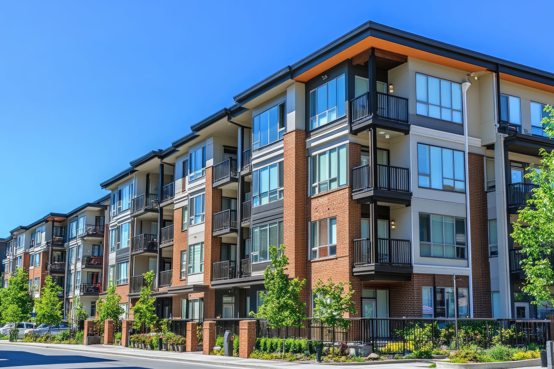 Multi-story apartment building with brick accents, balconies, and large windows under a blue sky.