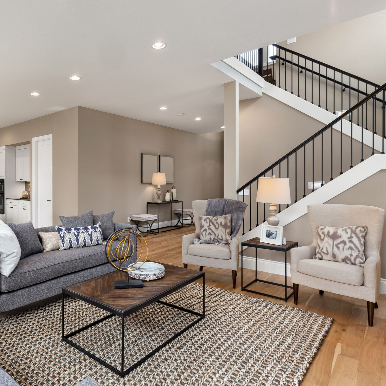 Living room with gray sofa, two armchairs, wooden coffee table, and staircase.