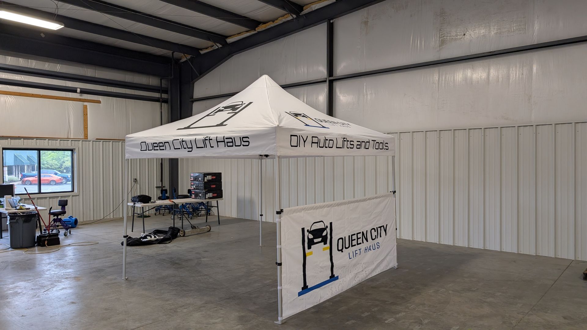 White branded event tent inside a warehouse with concrete floor and metal walls.