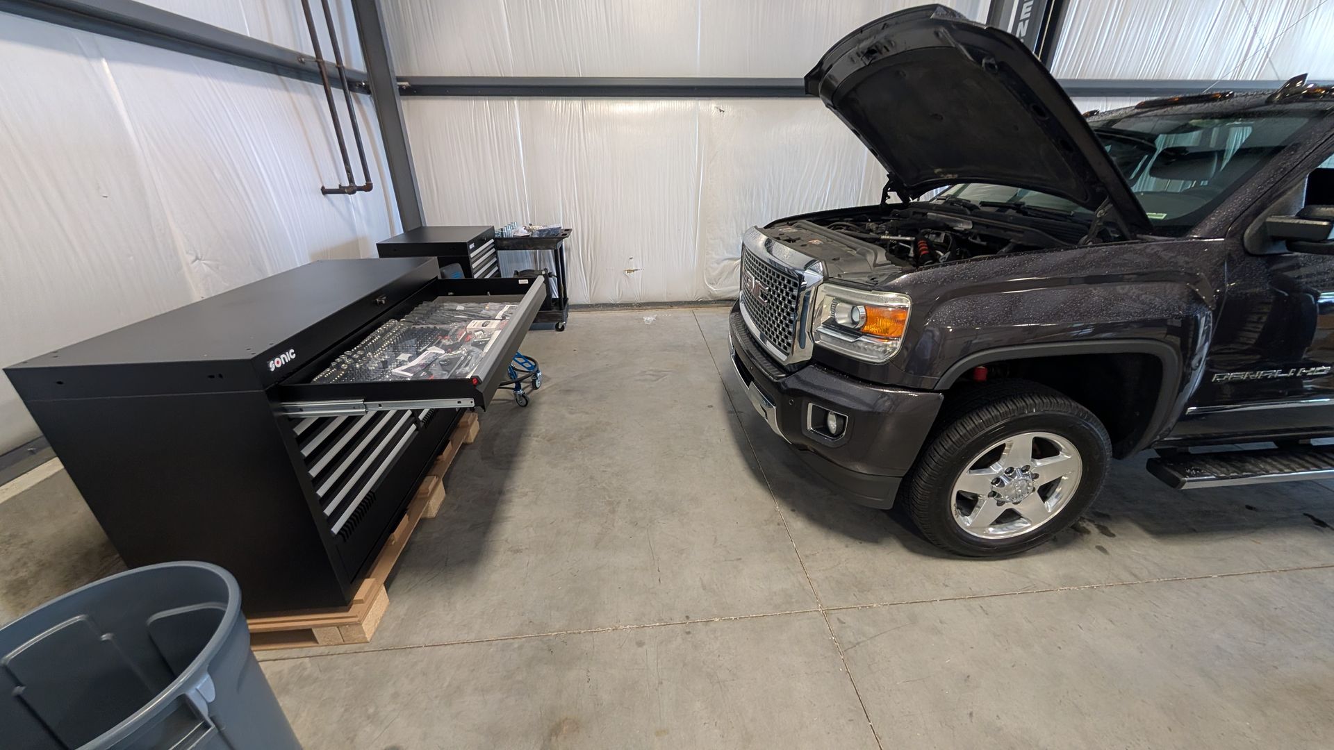 Black pickup truck with hood open beside a large tool chest in a garage.