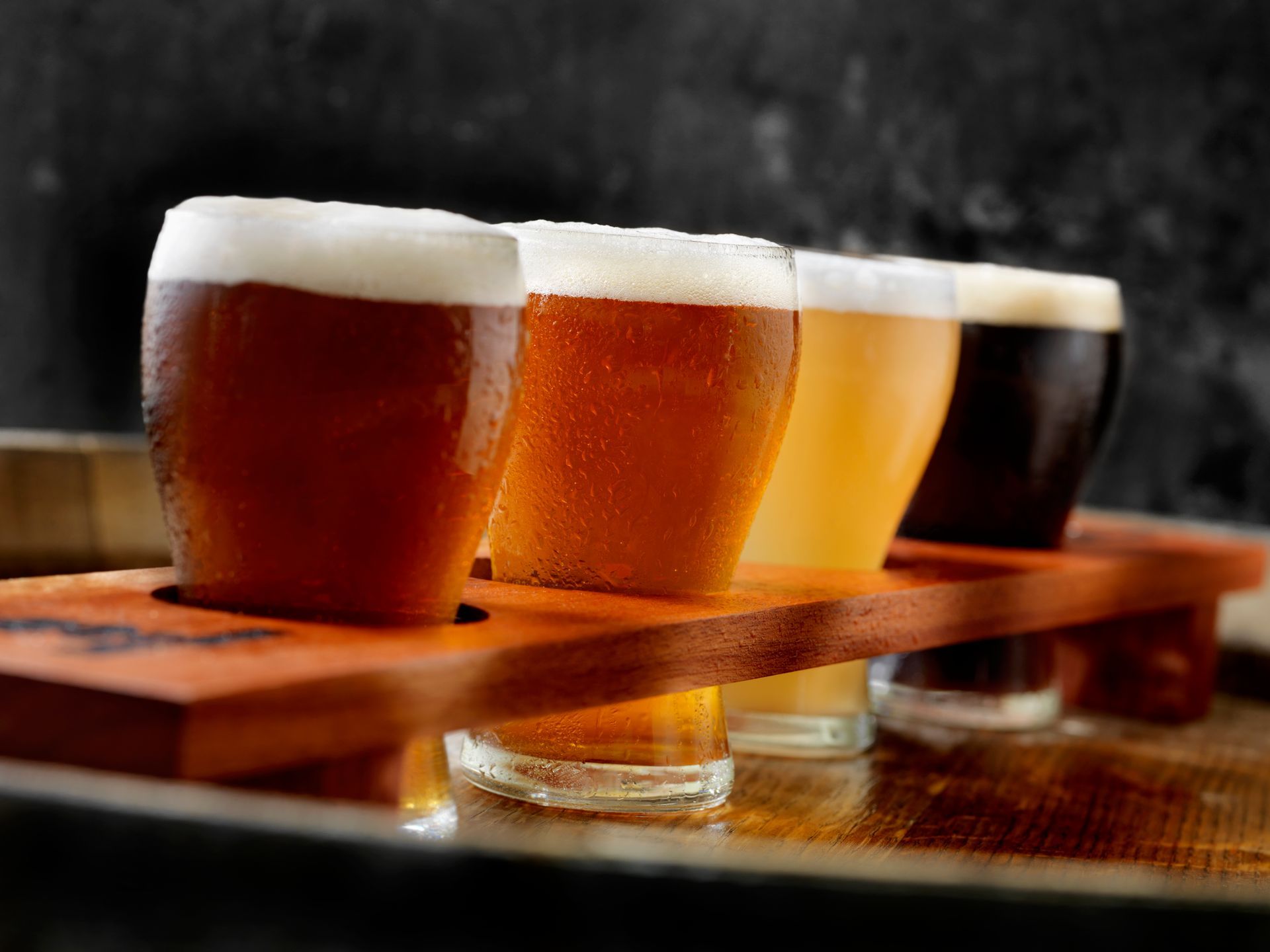 Quattro bicchieri di birra sono allineati su un vassoio di legno.