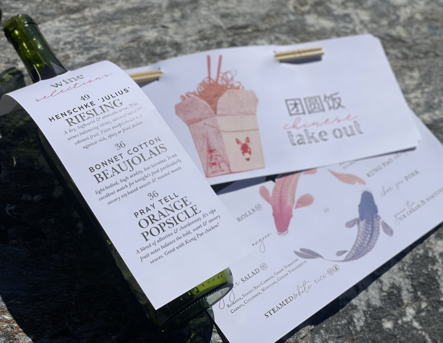 A wine bottle with a menu tag next to a Chinese takeout-themed card featuring illustrations of noodles and koi fish.