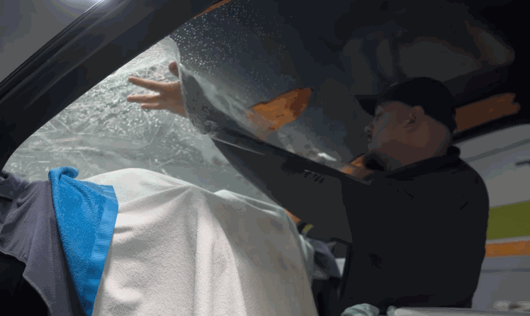 Installer reaches across the inside of a vehicle windshield to position window tint on wet glass during installation.