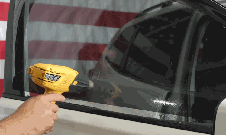 Installer uses a heat gun to shape window tint across the side window of a vehicle during installation.