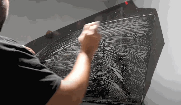 Installer cleans and prepares a vehicle window covered with soapy solution before applying window tint.