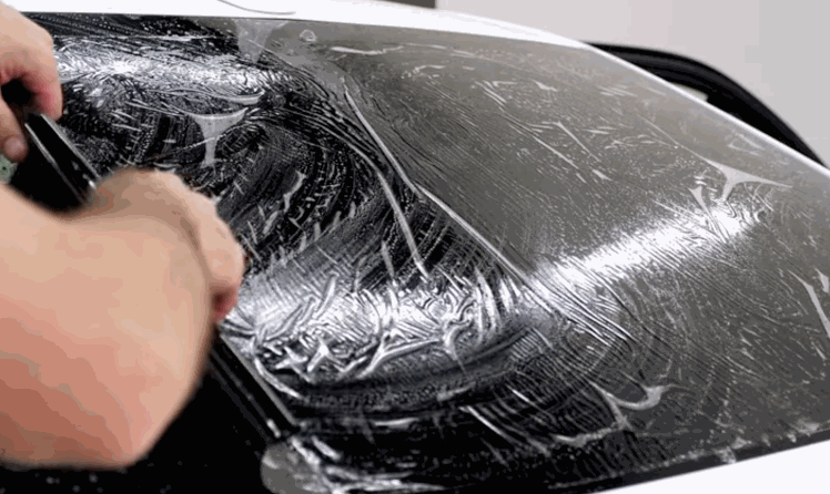 Installer uses a squeegee to smooth window tint across wet automotive glass covered with installation solution.
