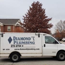 A white Diamond T Plumbing service van parked on a street in front of a house and a large tree.