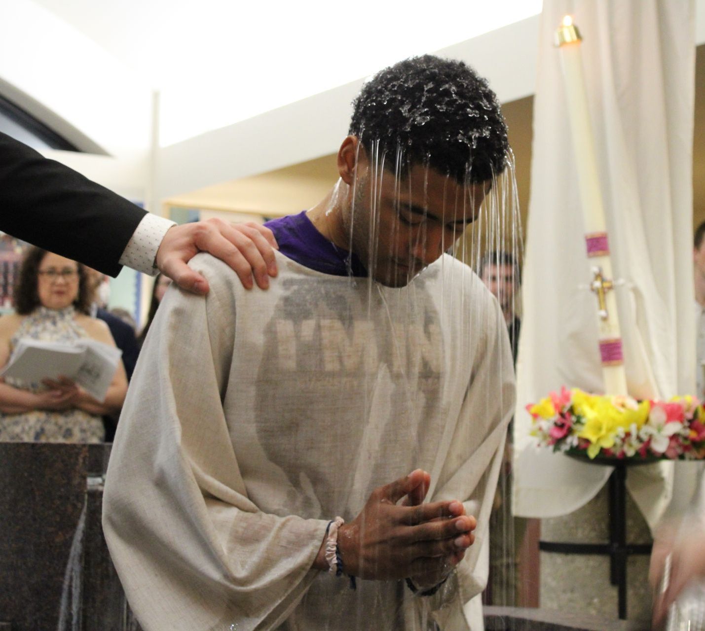 A man is being baptized with the word jesus on his shirt