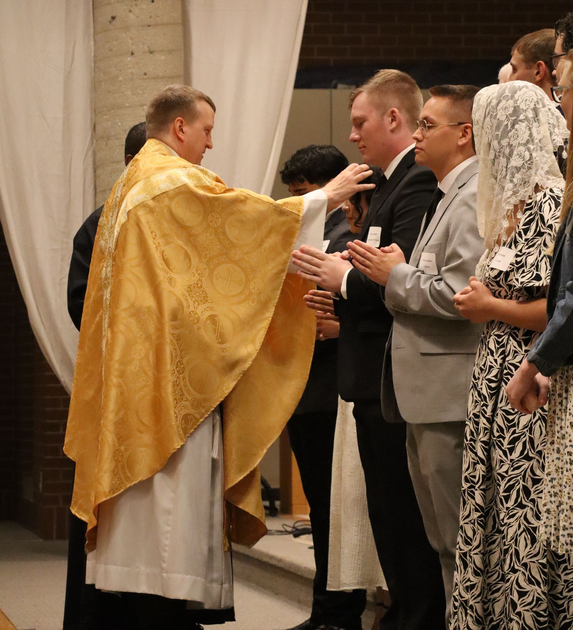 A man in a gold robe is standing in front of a group of people