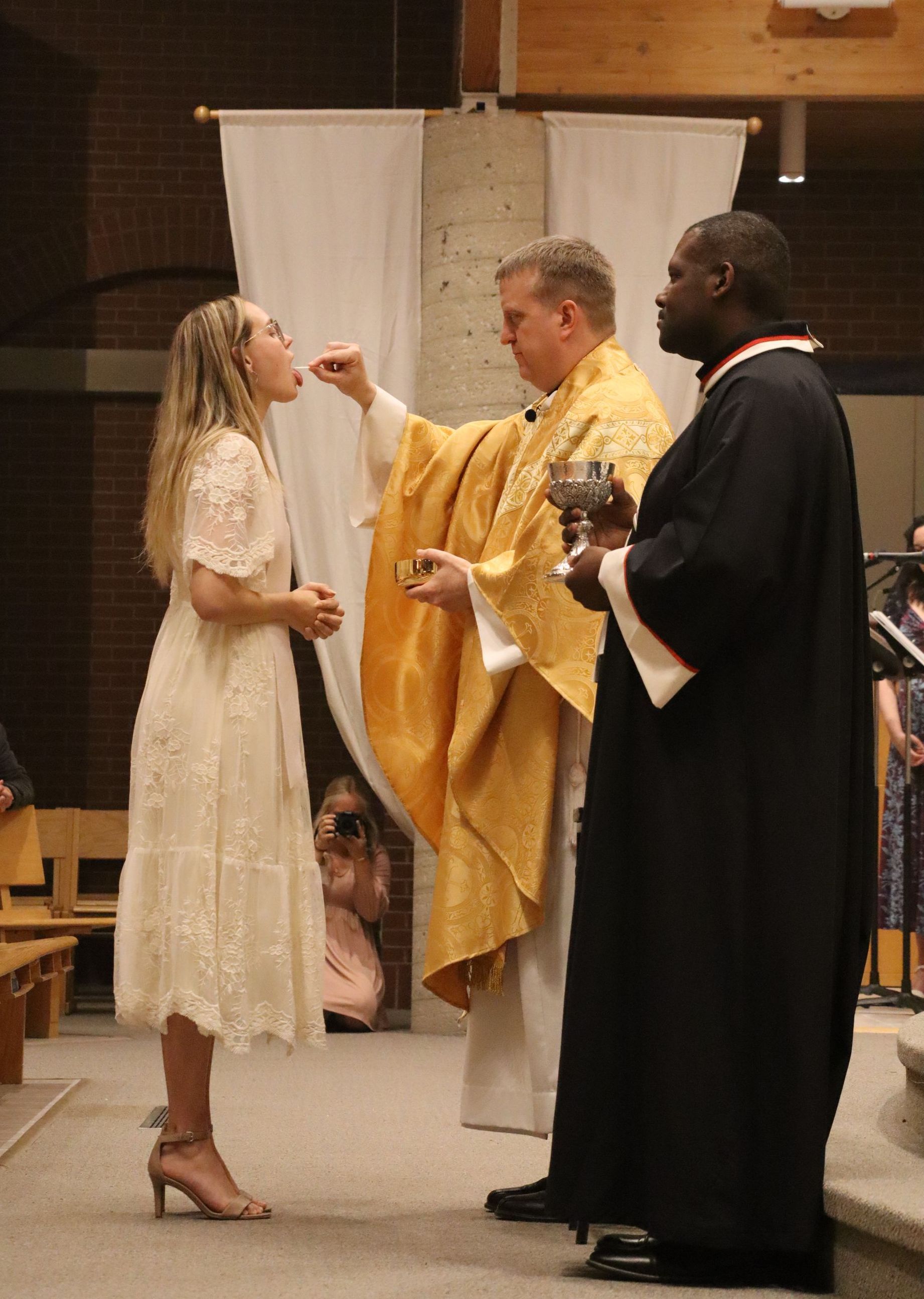 A woman in a white dress receiving holy communion for the first time