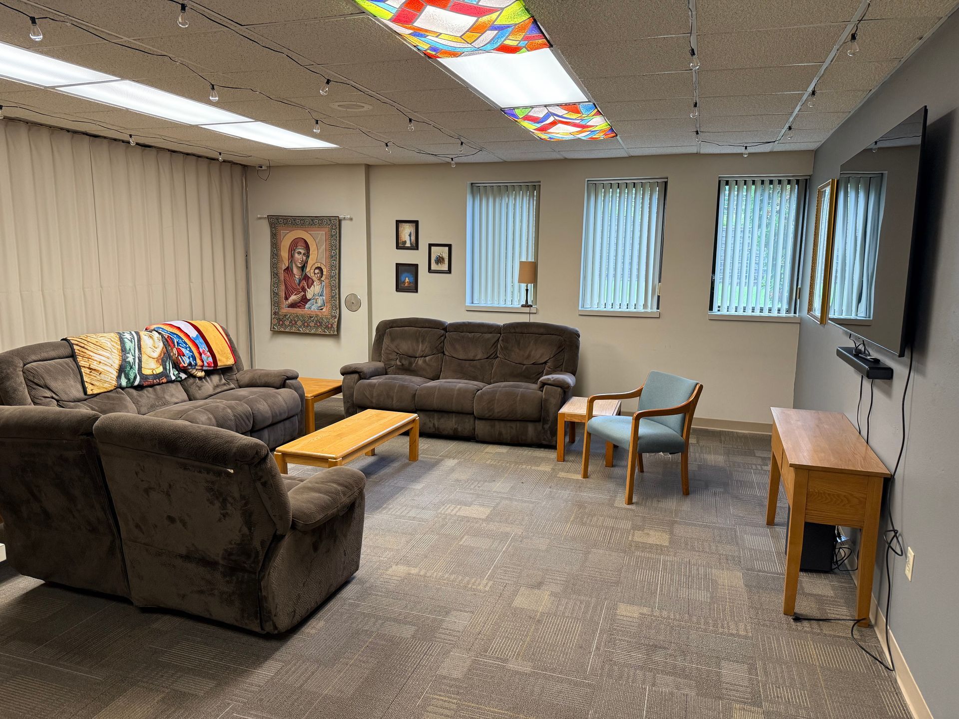 A lounge area with sofas, chairs, and a TV. Includes a colorful ceiling, windows, and a tapestry.