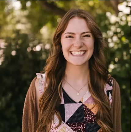 A young woman is smiling for the camera while standing in front of trees.