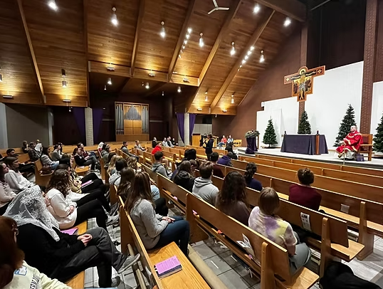 A group of people are sitting in a church with a crucifix in the background