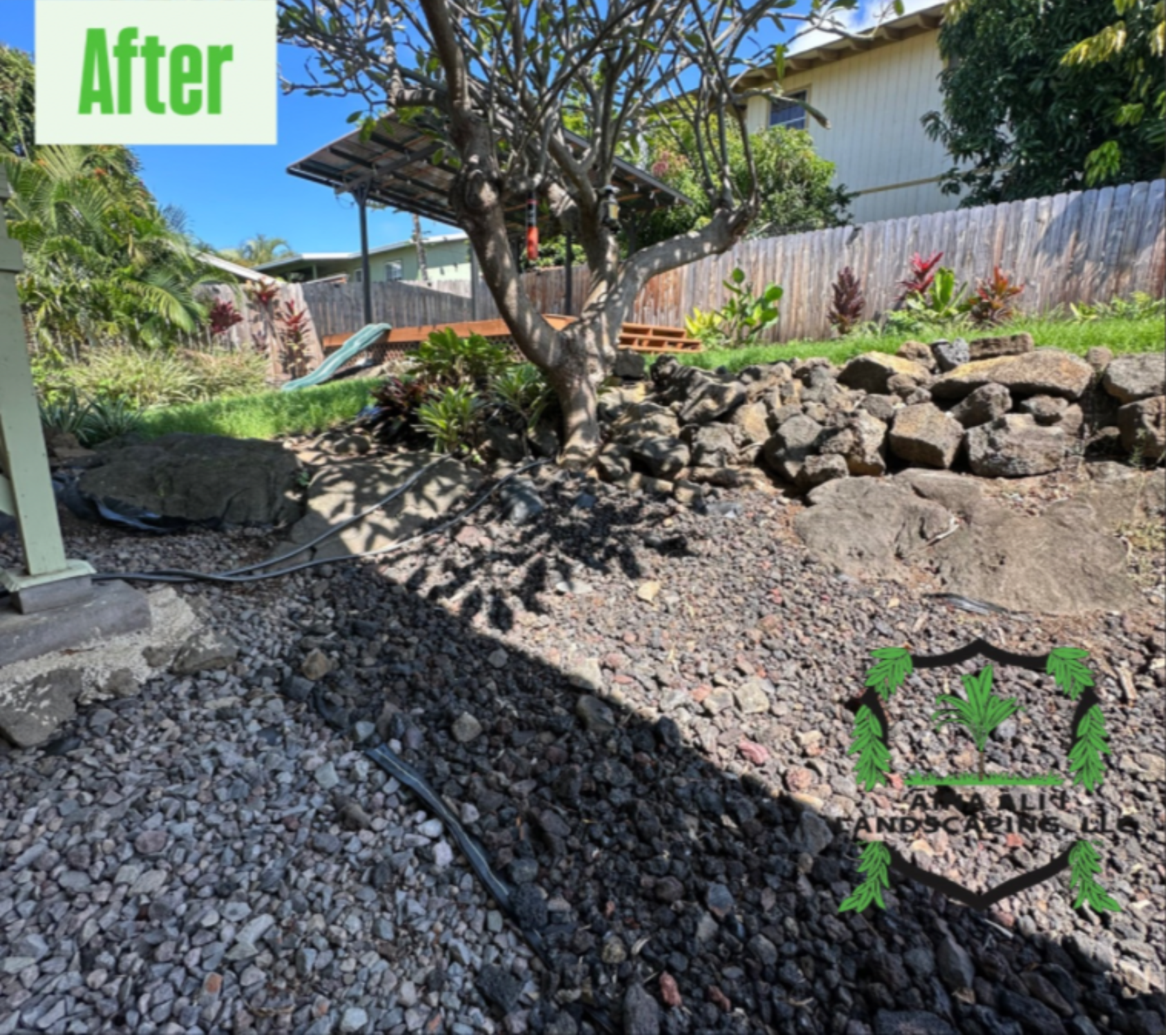 A landscaped backyard features a rocky slope, a central tree, wooden decking under a cover, and gravel ground cover.