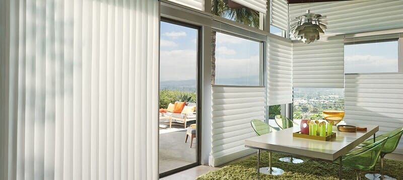 A modern dining area with horizontal and vertical white blinds covering large windows, next to a patio door.