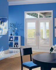 A modern dining area with blue walls, a dark circular table, and white French doors featuring plantation shutter blinds.