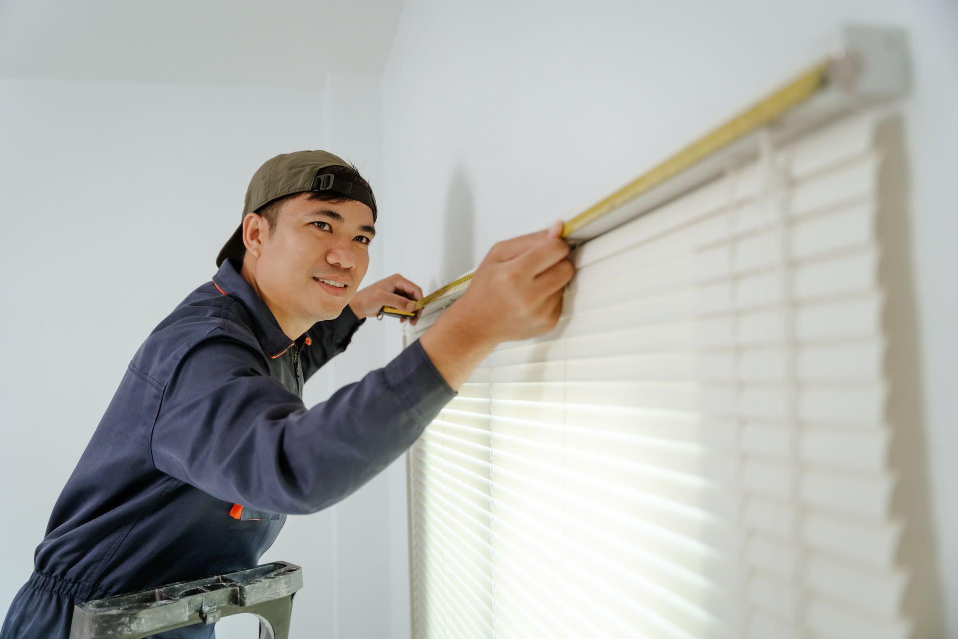 Professional installing custom blinds using measuring tape on window in residential space.
