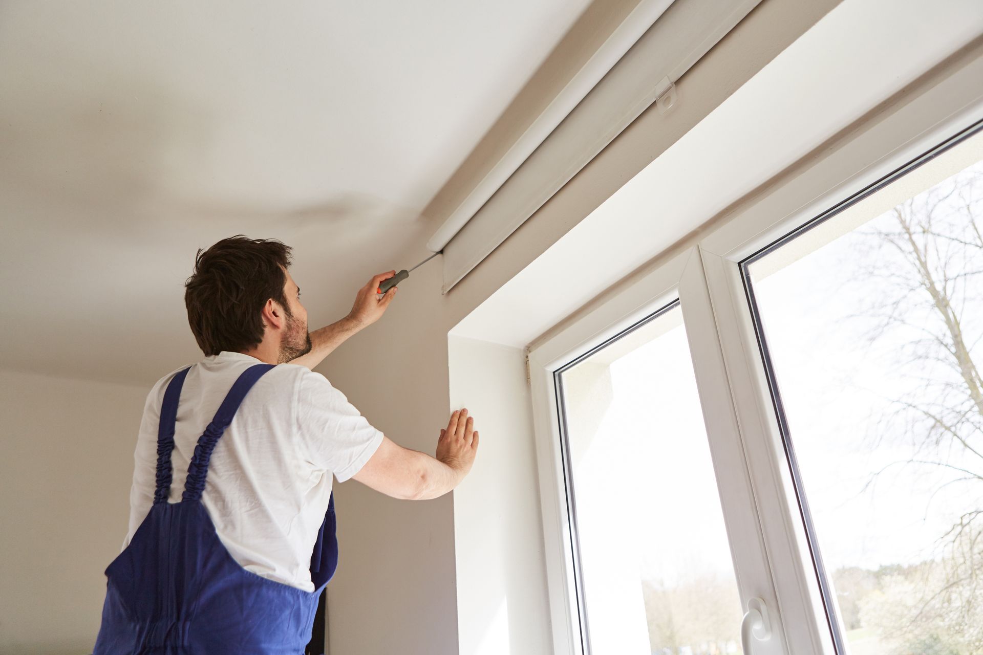 Technician performing blind installations on modern window frame inside bright home interior. Technician performing blind installations on modern window frame inside bright home interior.