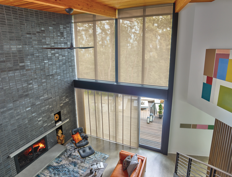 A modern living room with a tall stone fireplace, floor-to-ceiling windows, an orange sofa, and an abstract wall painting.