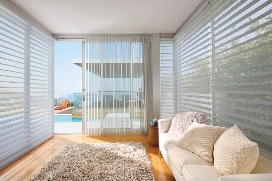 A bright, modern living room featuring a cream couch and shag rug, with large windows overlooking a pool and patio.