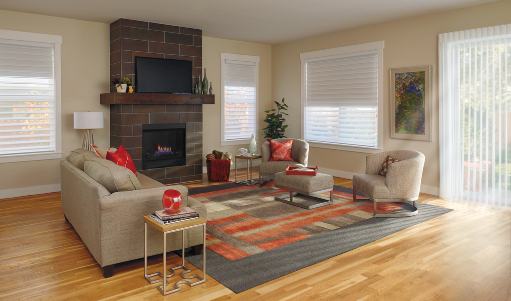 A living room with a brick fireplace, beige couch, armchairs, and a patterned rug on a hardwood floor.