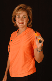 Woman in orange shirt smiles, holding a racquet, black background.