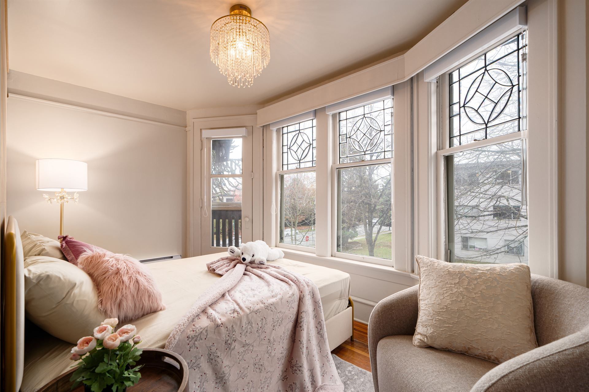 A bedroom with a bed , chair , lamp and lots of windows.