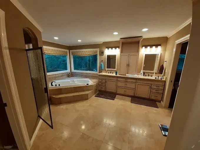 Spacious beige bathroom with corner soaking tub, double vanity, and large mirrors by windows