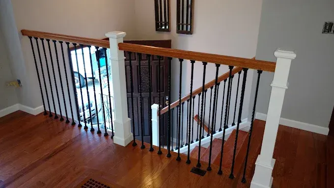 Interior staircase landing with wood floor, black balusters, and white railing posts