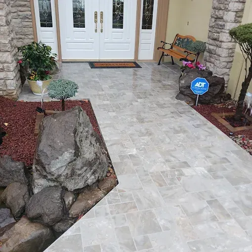 Stone walkway leading to a white front door, with landscaped beds and a bench by the entrance.