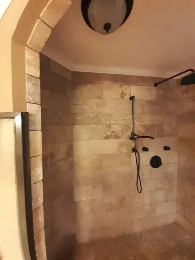 Stone-tiled walk-in shower with dark fixtures and curved archway
