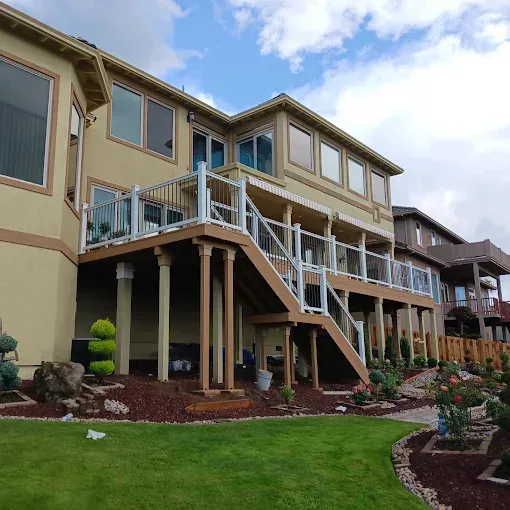 Two-story beige apartment building with exterior staircases and landscaped lawn under a cloudy sky