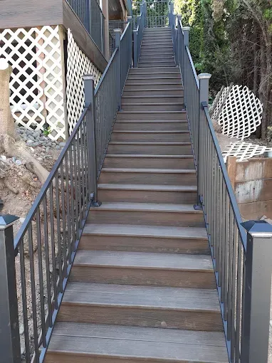 Steep outdoor staircase with black railings leading up between stone walls and lattice panels