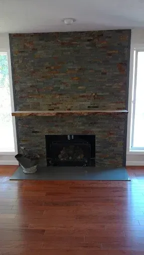 Stone fireplace with dark wooden mantel in a room with hardwood floors and windows on either side