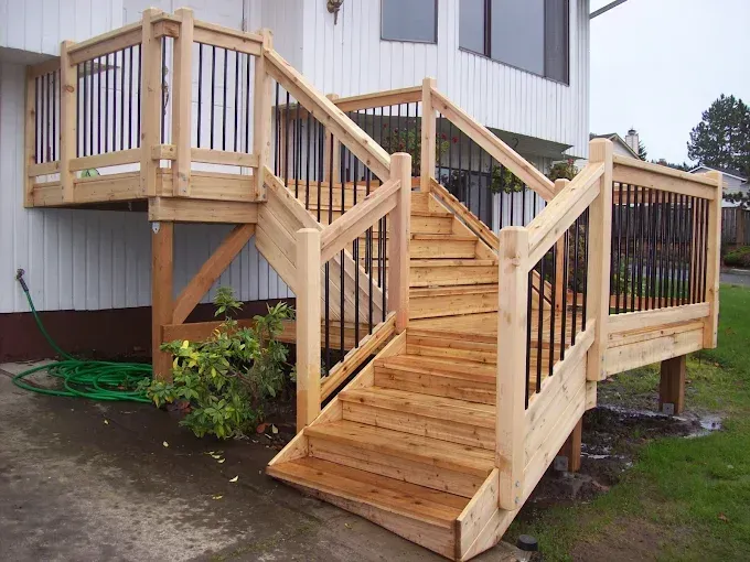 Wooden accessibility ramp and stairs leading to a house entrance, with railings and wet ground nearby