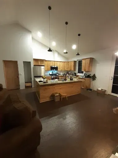 Open kitchen and living room with pendant lights, wooden cabinets, and dark wood floors.