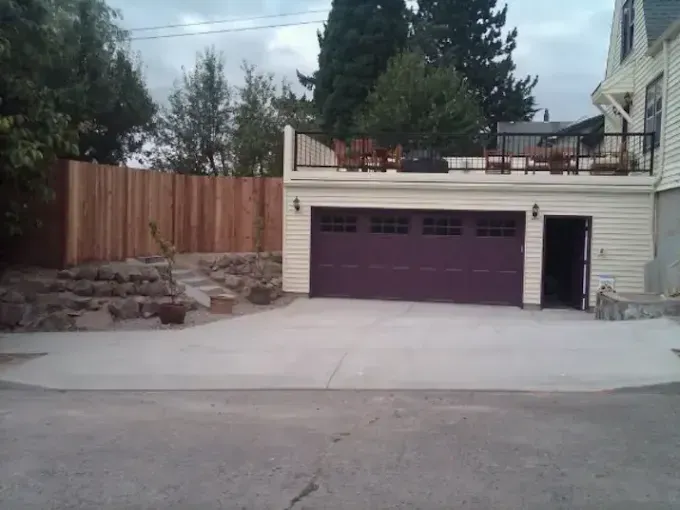 Detached garage with purple doors, driveway, and fenced yard beside a house