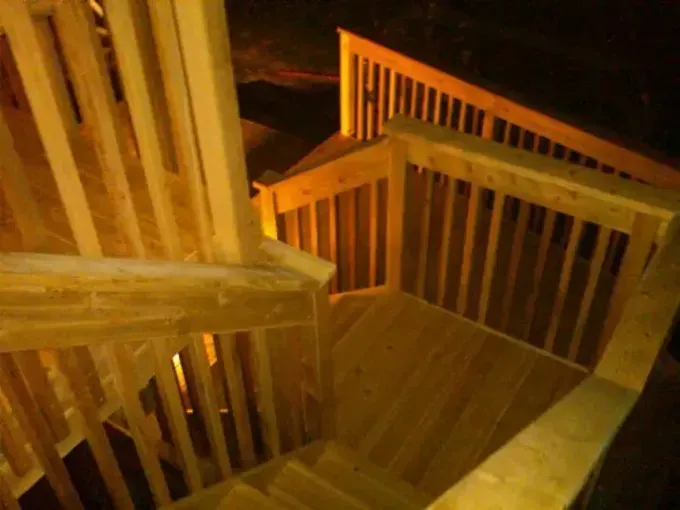 Wooden outdoor staircase and railing lit by warm yellow light at night