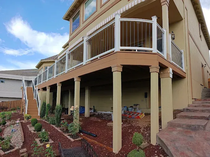 Raised deck and staircase on a beige house with a landscaped yard underneath
