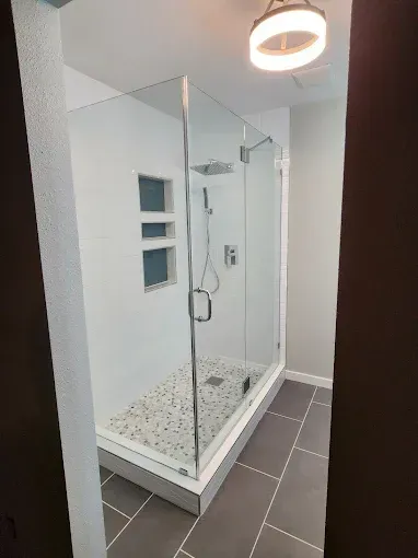 Modern bathroom with a glass-enclosed shower, white walls, and gray tile floor.