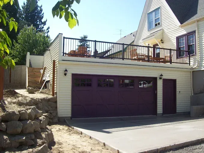 Two-car garage with purple doors and a rooftop deck beside a stone retaining wall