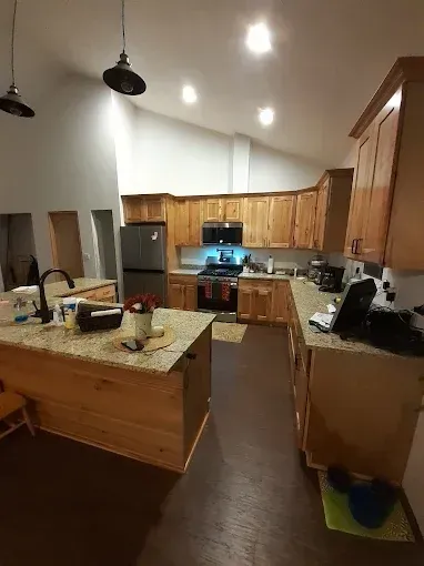 Modern kitchen with wooden cabinets, granite island, and stainless steel appliances under recessed lights