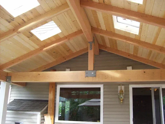 Wooden porch ceiling with exposed beams, skylights, and a center support post above sliding glass doors