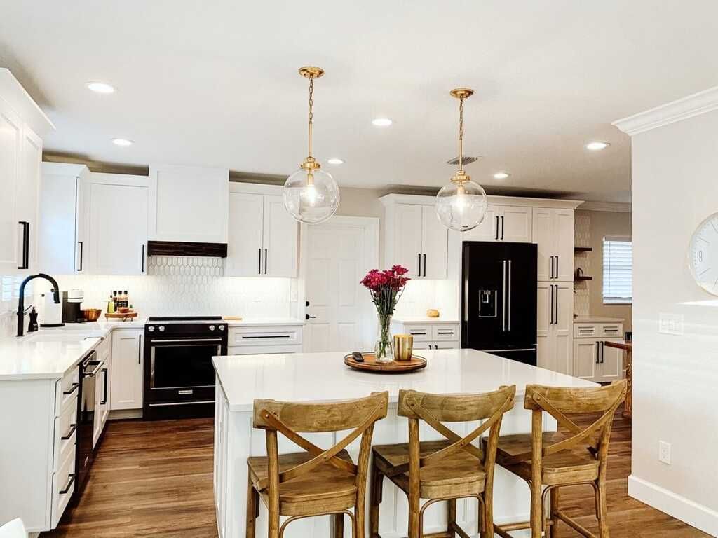 White kitchen with island, stools, overhead lights, and black appliances.
