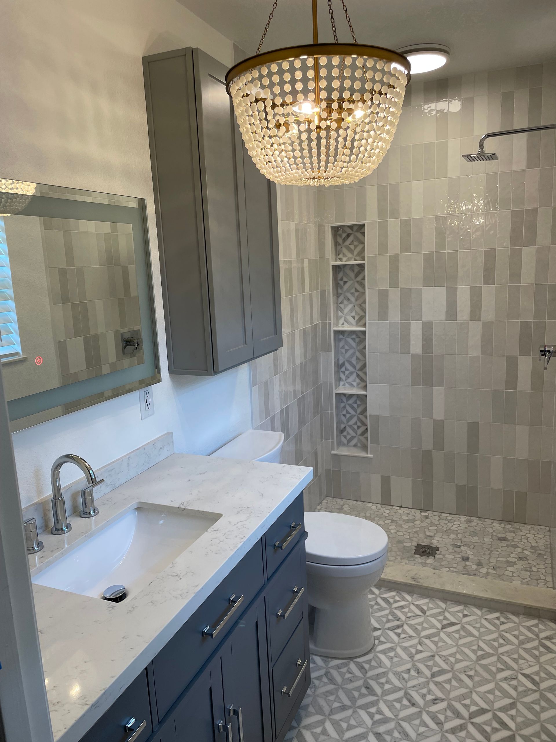 Gray and white bathroom with a marble countertop vanity, shower, and a chandelier.