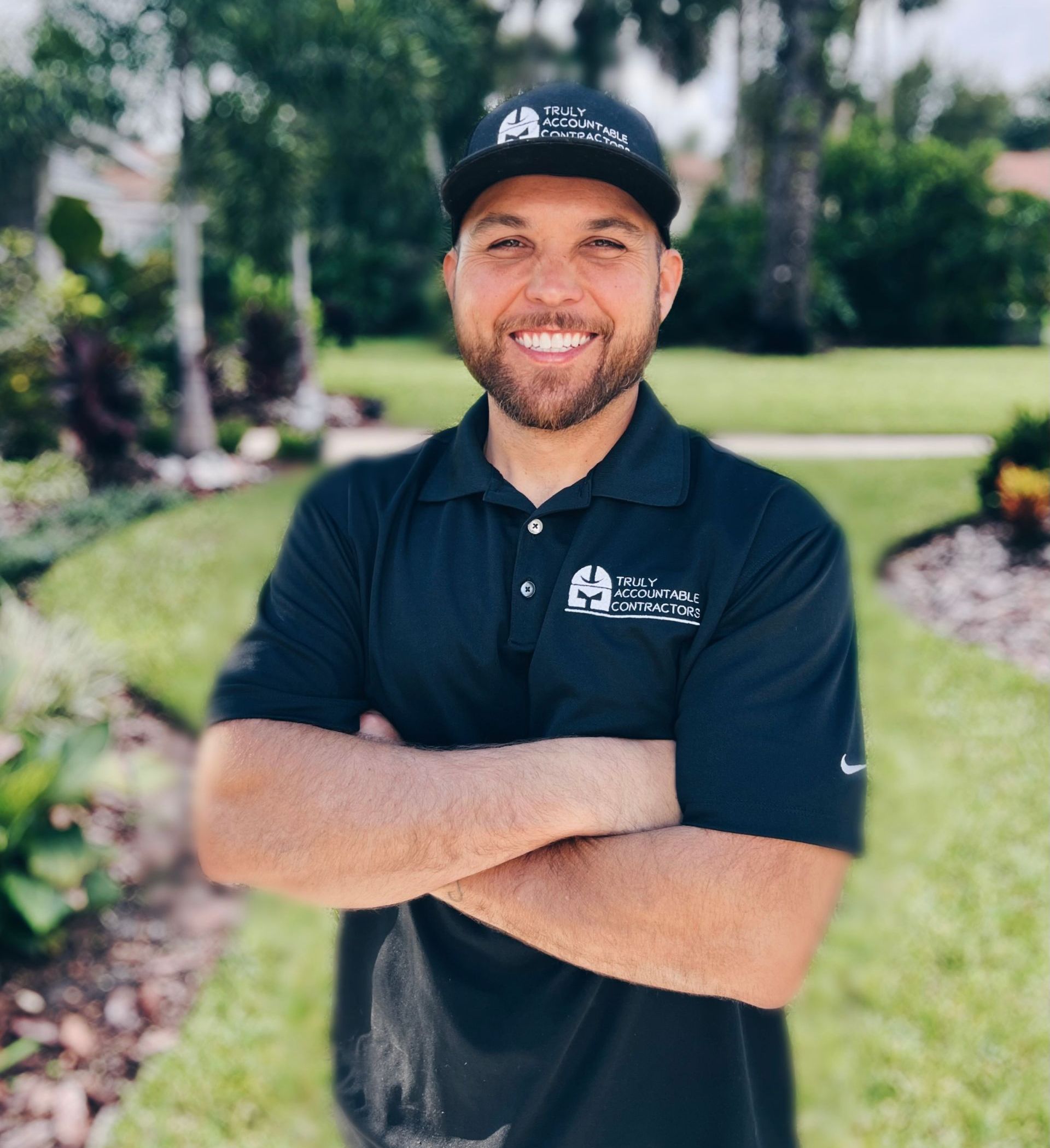 Man in black uniform smiles with arms crossed, outdoors.